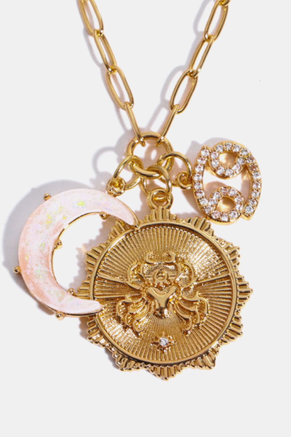 Gold celestial pendant necklace with Cancer zodiac, moon charm, and sunburst detail.