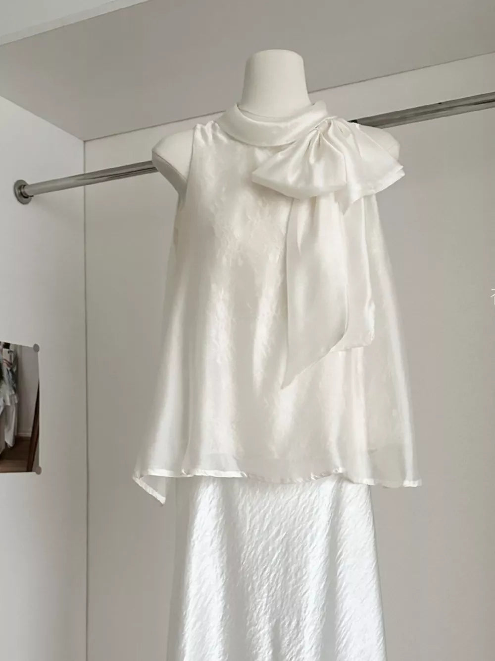 Sleeveless white shirt with a large bow detail on the shoulder and a textured fabric.
