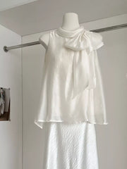 Sleeveless white shirt with a large bow detail on the shoulder and a textured fabric.
