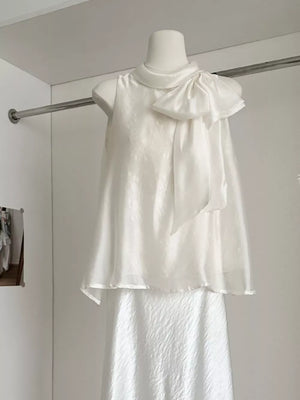 Sleeveless white shirt with a large bow detail on the shoulder and a textured fabric.