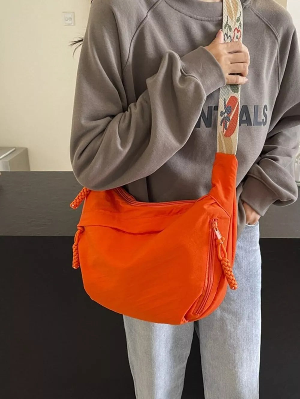 Orange woven strap small crossbody bag with braided zipper pulls and a colorful graphic strap.