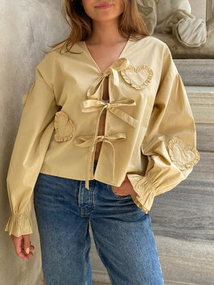 Pastel yellow blouse with heart appliqués and tie front, featuring ruffled cuffs and V-neck.