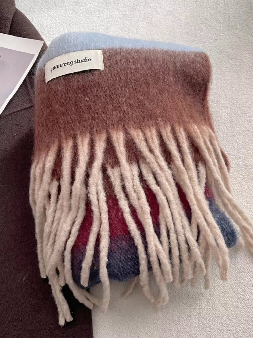 Plush multi-patterned scarf with cream tassels, featuring brown, blue, and red stripes.