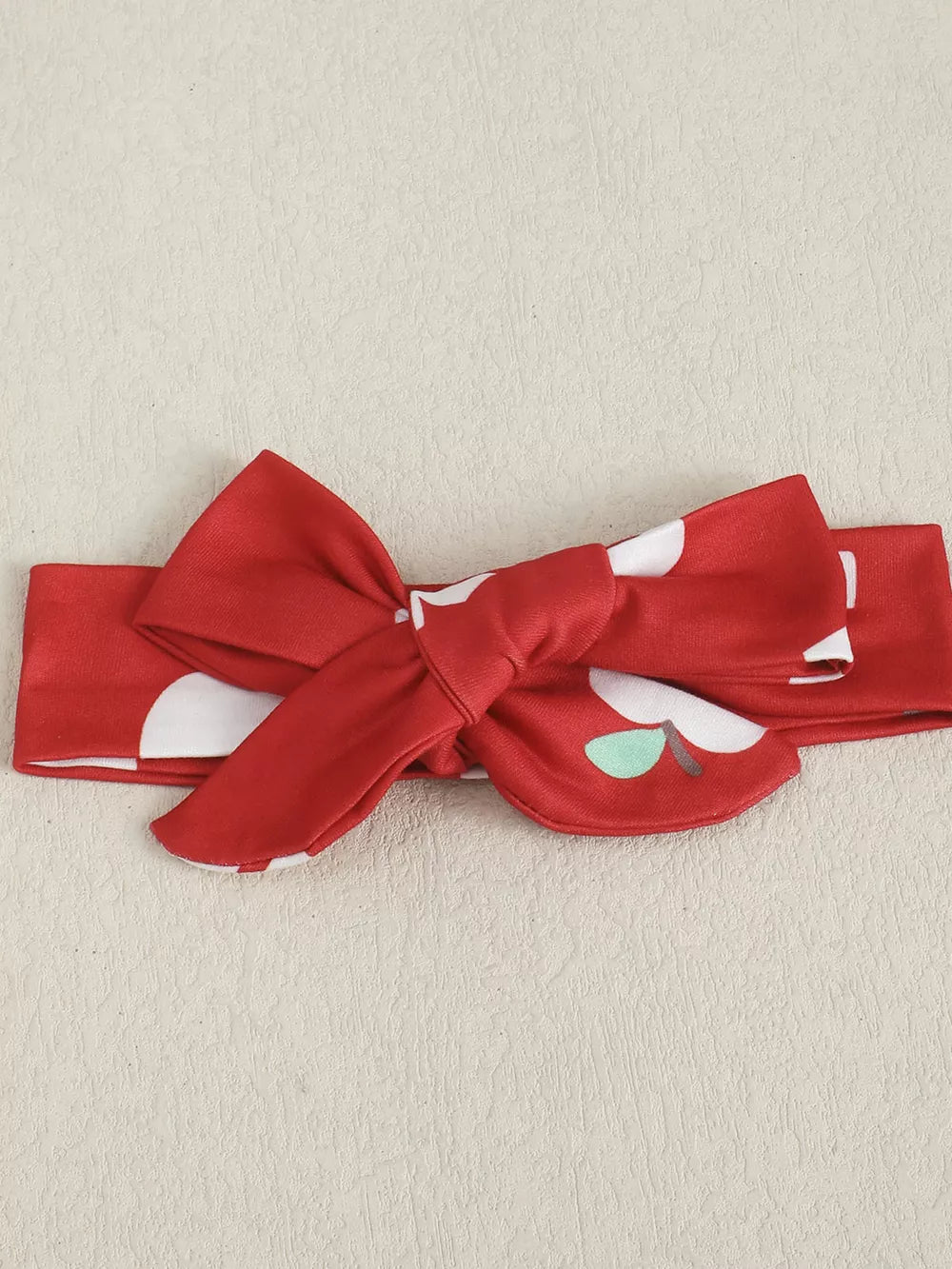 Red baby headband with white polka dots and apple print, featuring a bow.