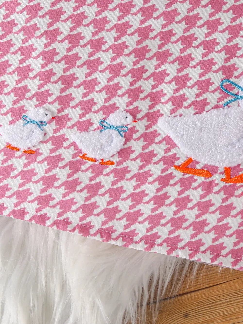 Pink houndstooth baby bodysuit with embroidered ducklings and blue bows.