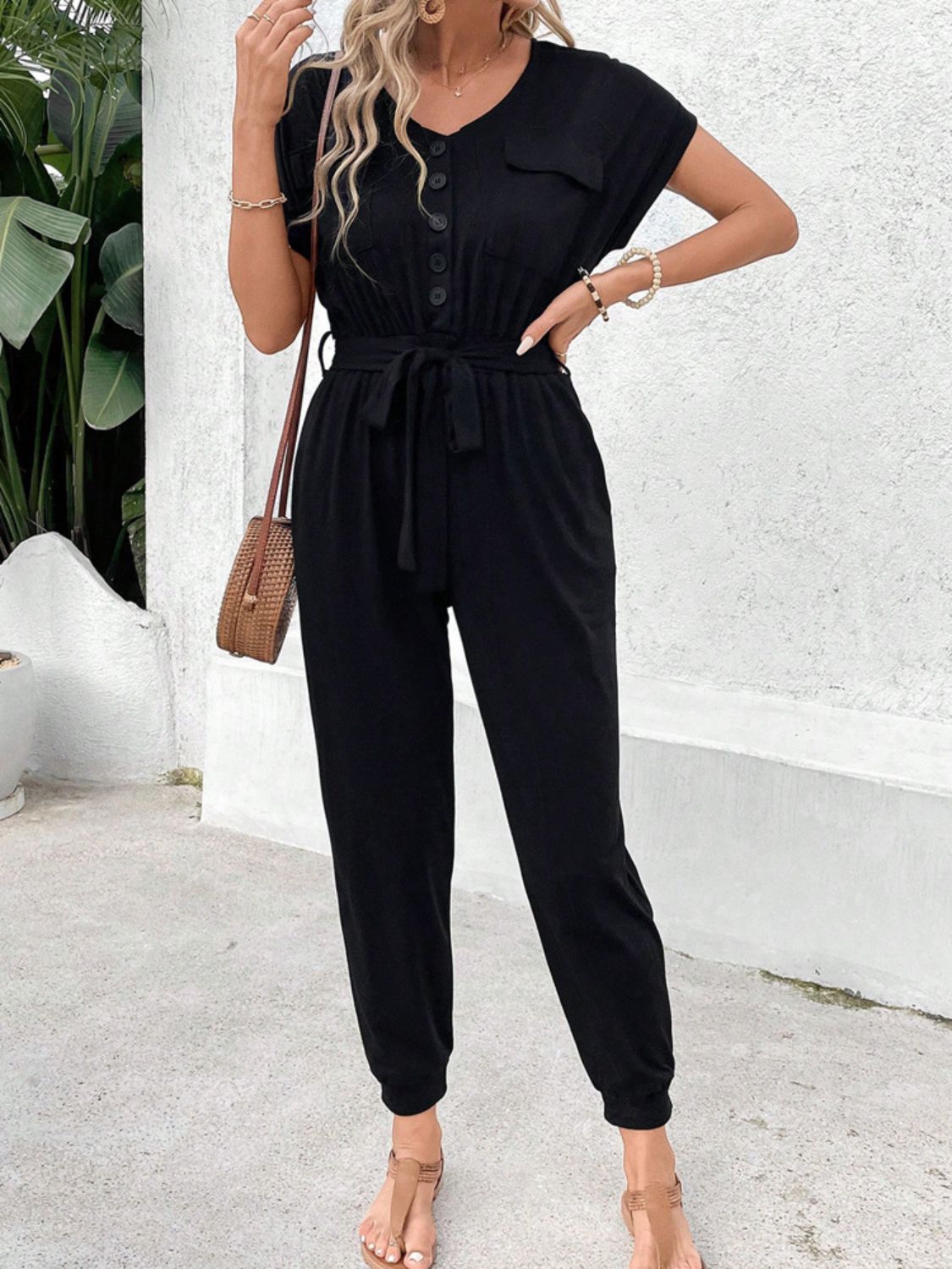 Black utility jumpsuit with short sleeves, V-neck, button front, tie waist, and pockets.