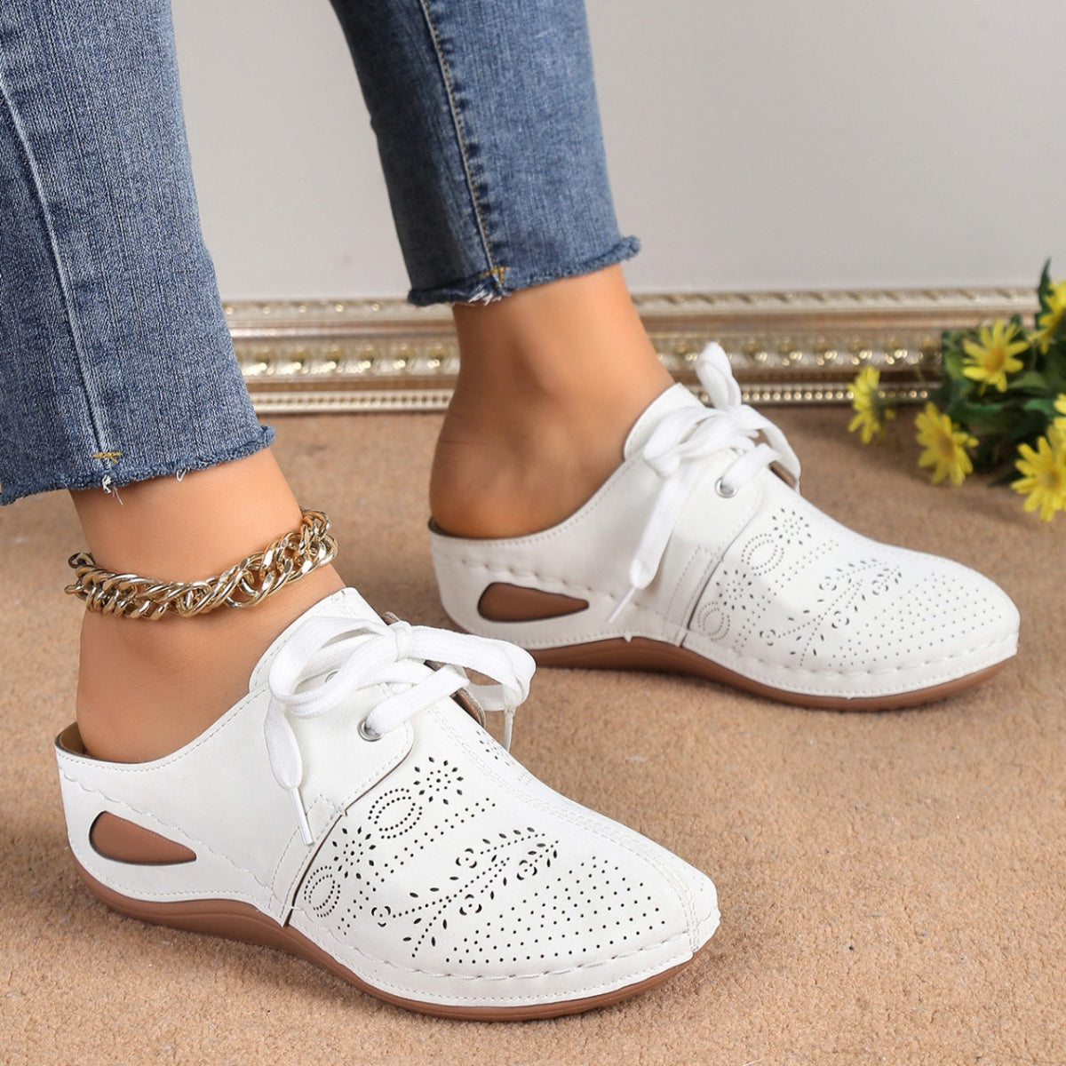 White perforated slip-on mules with decorative lacing and cut-out sides.