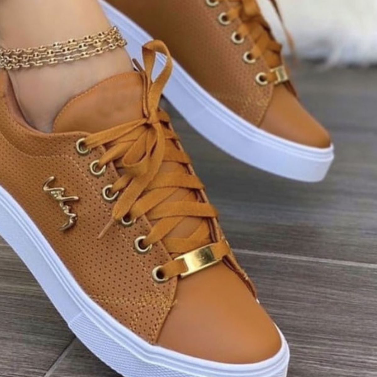 Brown perforated lace-up sneakers with gold accents and white soles.