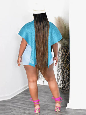 Light blue oversized cape shirt with pleated texture and abstract print, polyester, worn with denim shorts.