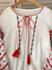 White folk-inspired shirt with red tie neck, tassels, and embroidered details.