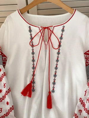 White folk-inspired shirt with red tie neck, tassels, and embroidered details.