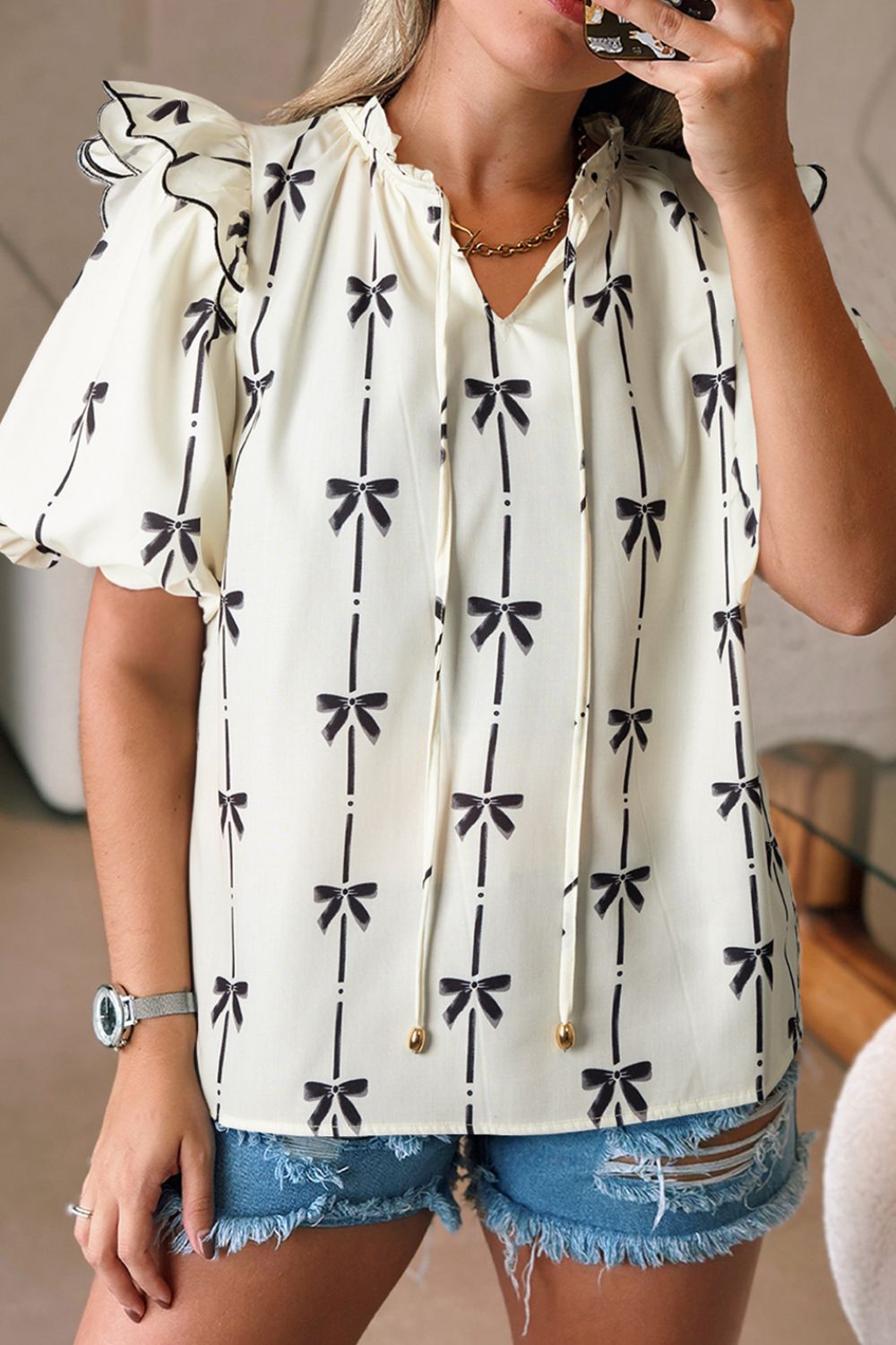 Ivory blouse with black bow print, ruffled sleeves, and tie neckline.