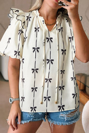Ivory blouse with black bow print, ruffled sleeves, and tie neckline.