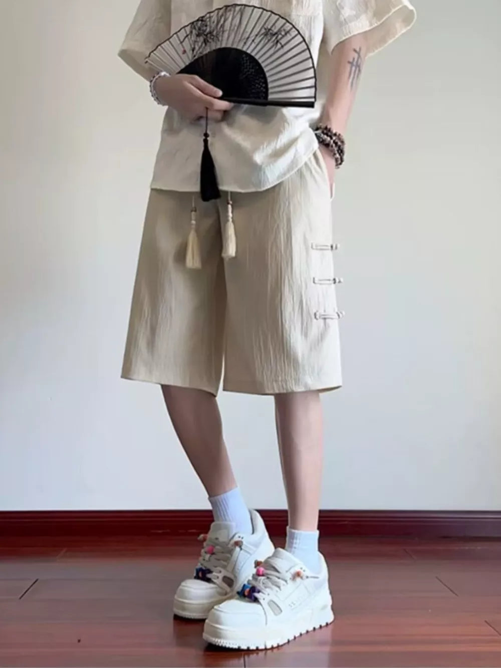 Beige chino shorts with drawstring and decorative side buttons.