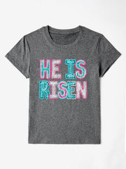 Gray crewneck t-shirt with sequin-textured "He Is Risen" graphic in pink and aqua.