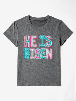 Gray crewneck t-shirt with sequin-textured "He Is Risen" graphic in pink and aqua.