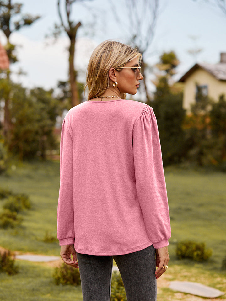 Pink ruffled henley sleeve blouse with gathered shoulder detail.