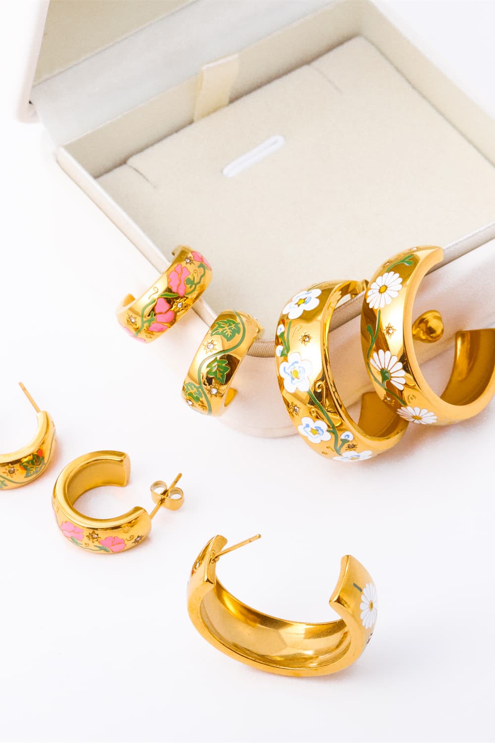Gold hoop earrings with floral enamel details in pink, green, and white daisy designs.