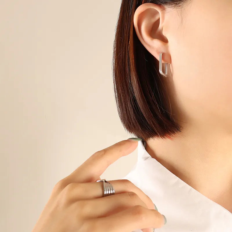 Silver Wide Triangle huggie earrings made of steel, worn by a woman.