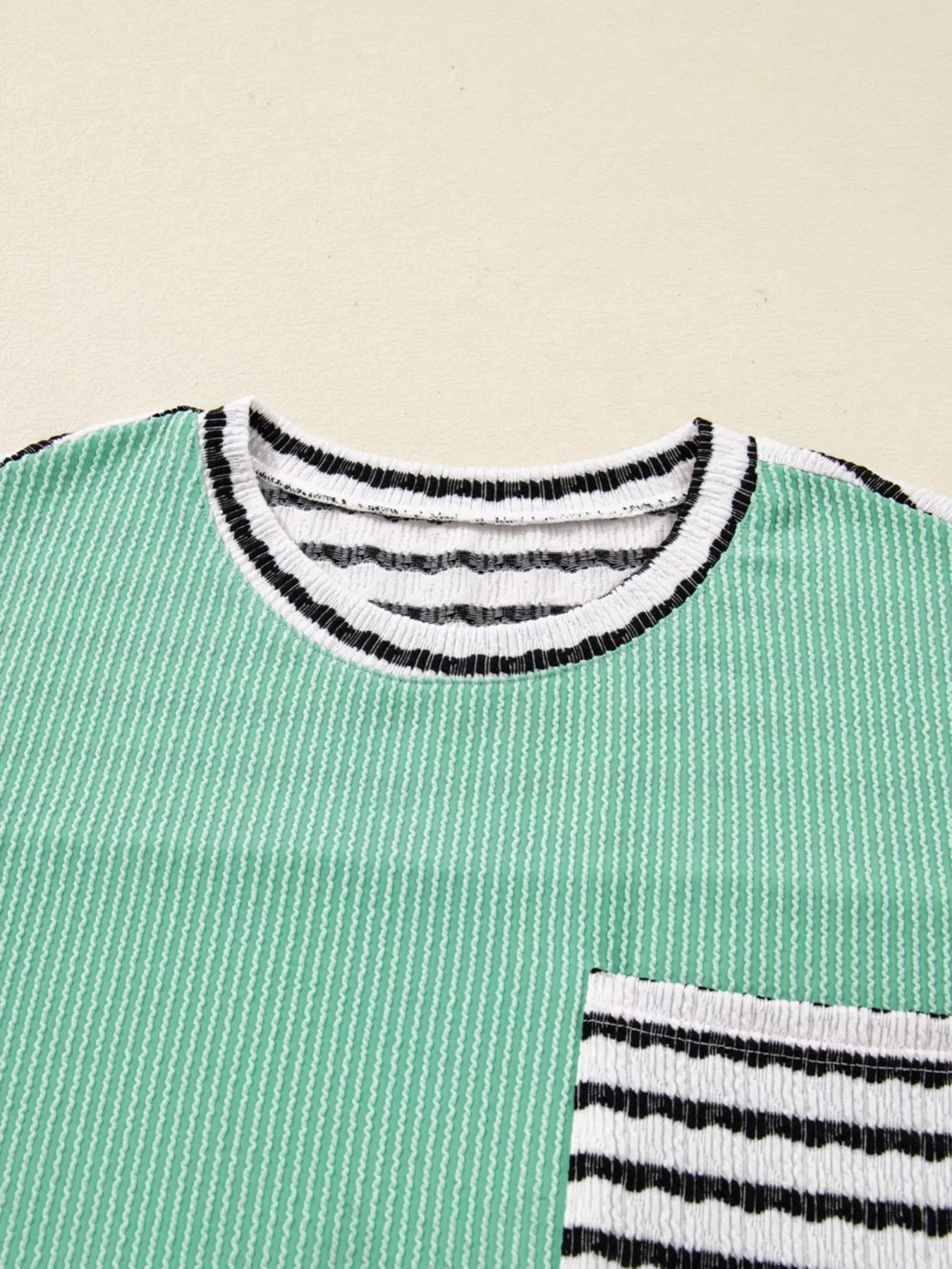 Turquoise twisted ribbed long-sleeve top with striped neckline and pocket detail.