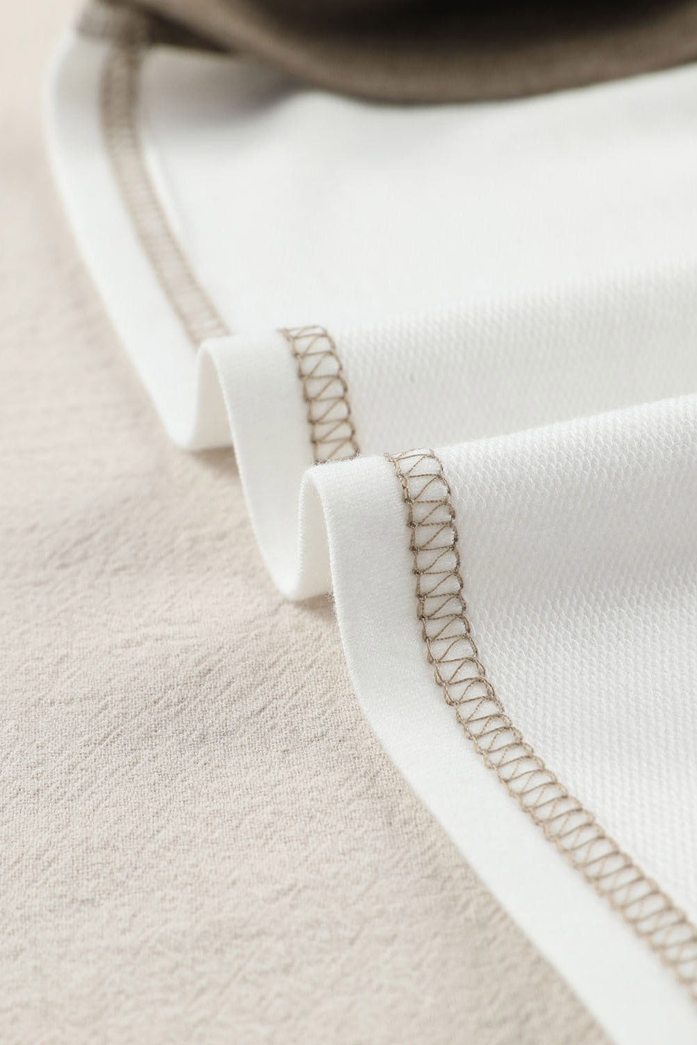 Colorblock knit top in white with tan contrast stitching detail.
