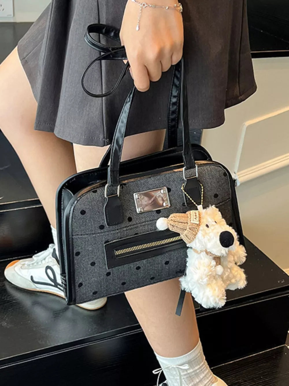 Sophisticated black polka dot shoulder bag with a zippered pocket and a plush dog charm.
