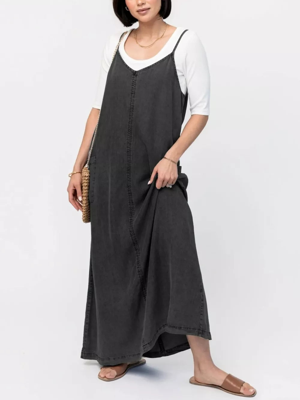 Black denim maxi dress with adjustable straps and V-neck, styled with a white tee.