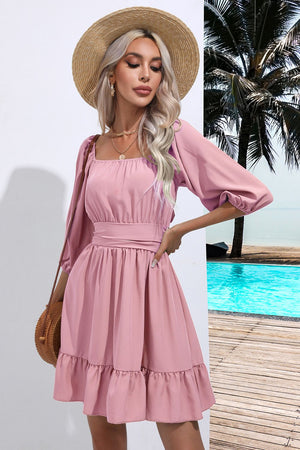 Blush pink mini dress with square neck, tie waist, ruffled hem, and puff sleeves.