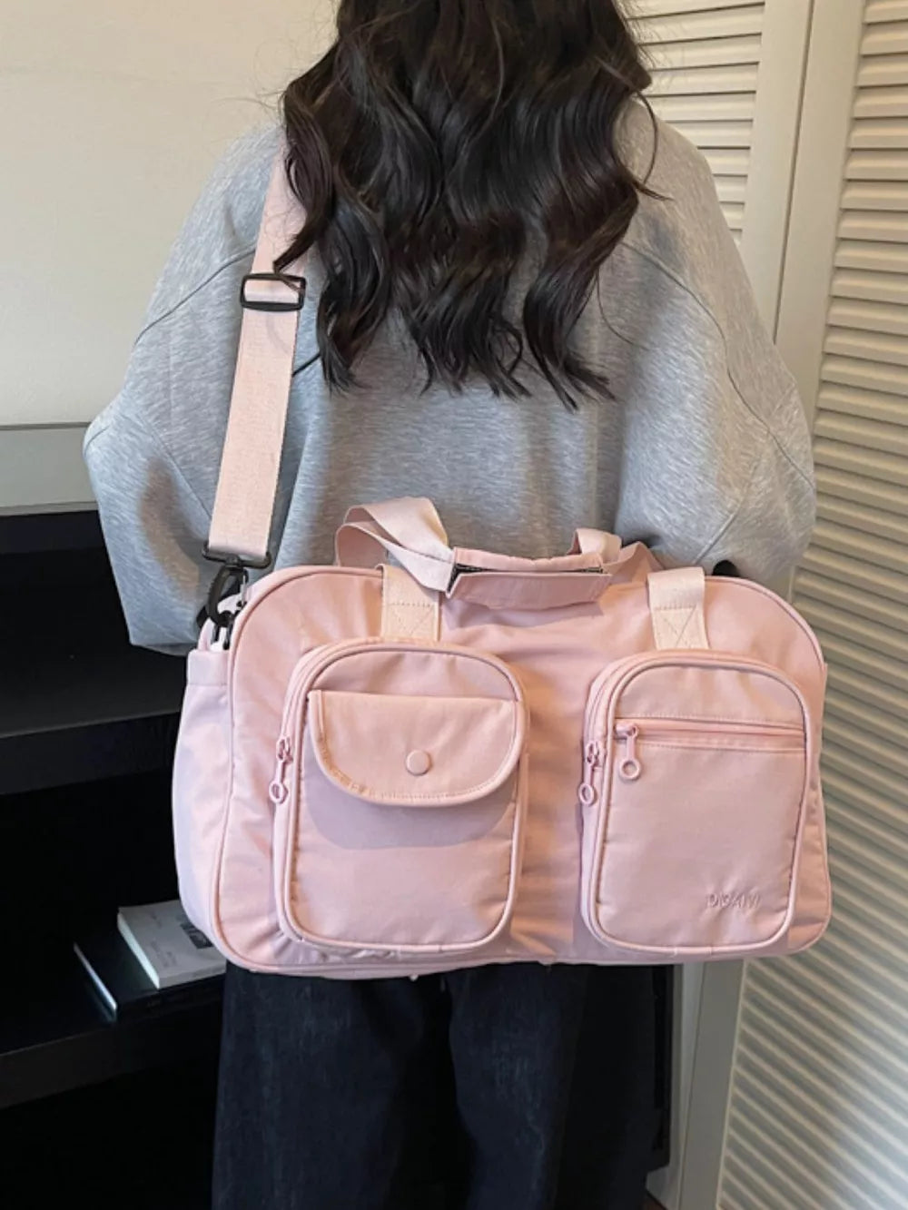 Pink nylon duffle bag with multiple front pockets and adjustable strap.