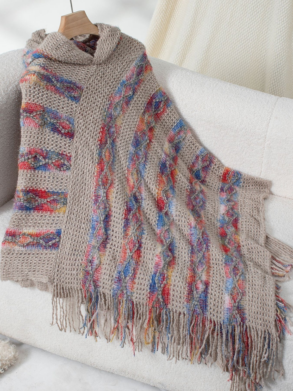 Textured knit hooded cape in tan with colorful diamond pattern and fringe.