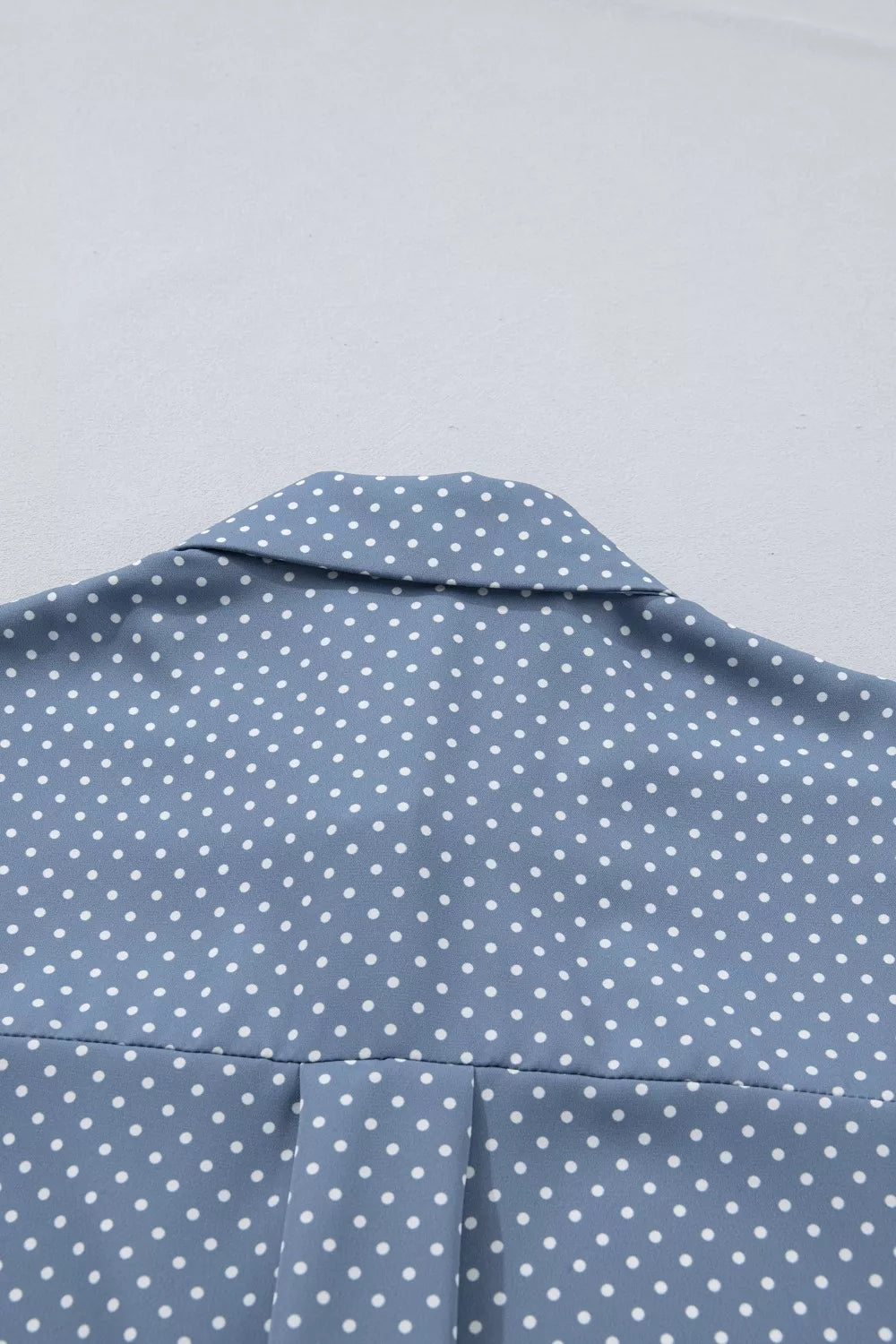 Blue polka dot polyester shirt with a collared neckline and subtle pleating detail.