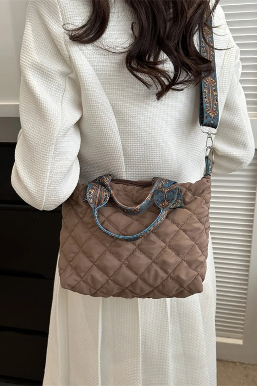 Quilted satchel bag in taupe with a patterned strap and handles.