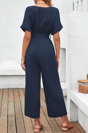 Navy crossover neckline fluid wide leg jumpsuit with belted waist and short sleeves.