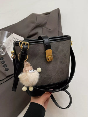 Elegant bucket bag in dark brown PU leather with gold hardware and a cute fuzzy charm.