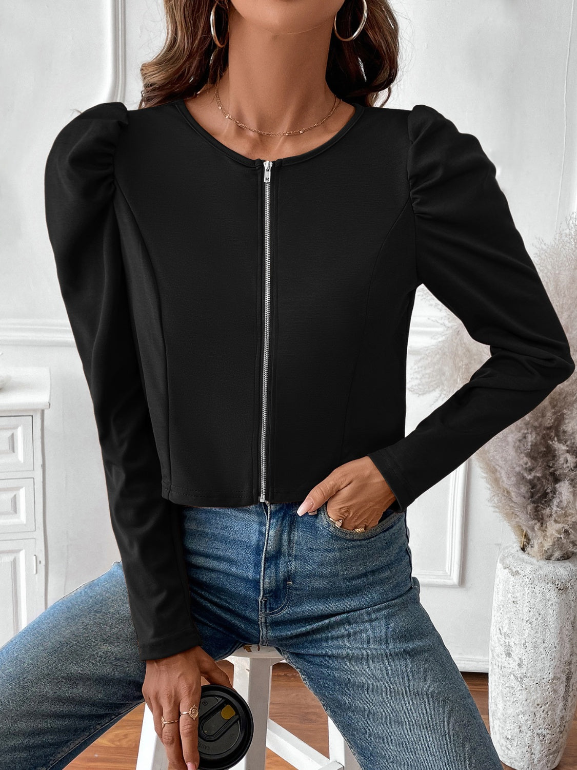 Black zip-front bolero jacket with puffed long sleeves and a round neckline.