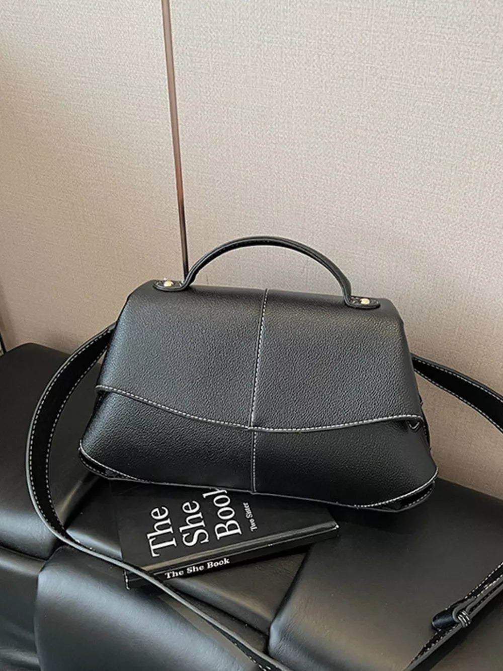 Black textured geometric flap shoulder bag with white contrast stitching and top handle.