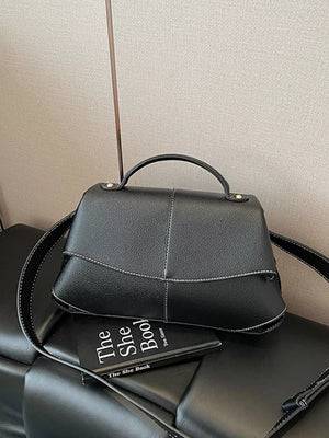 Black textured geometric flap shoulder bag with white contrast stitching and top handle.