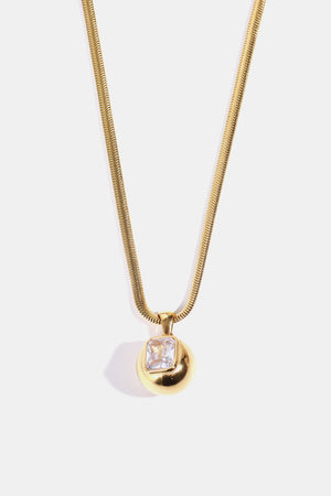 Gold necklace with a sculpted orb pendant featuring a transparent square stone.