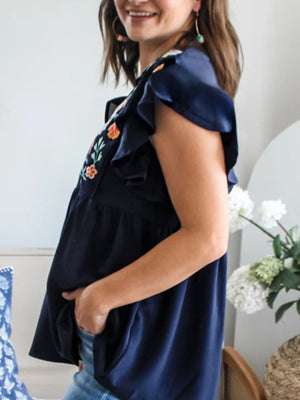 Navy embroidered floral blouse with ruffle sleeves and a babydoll cut.