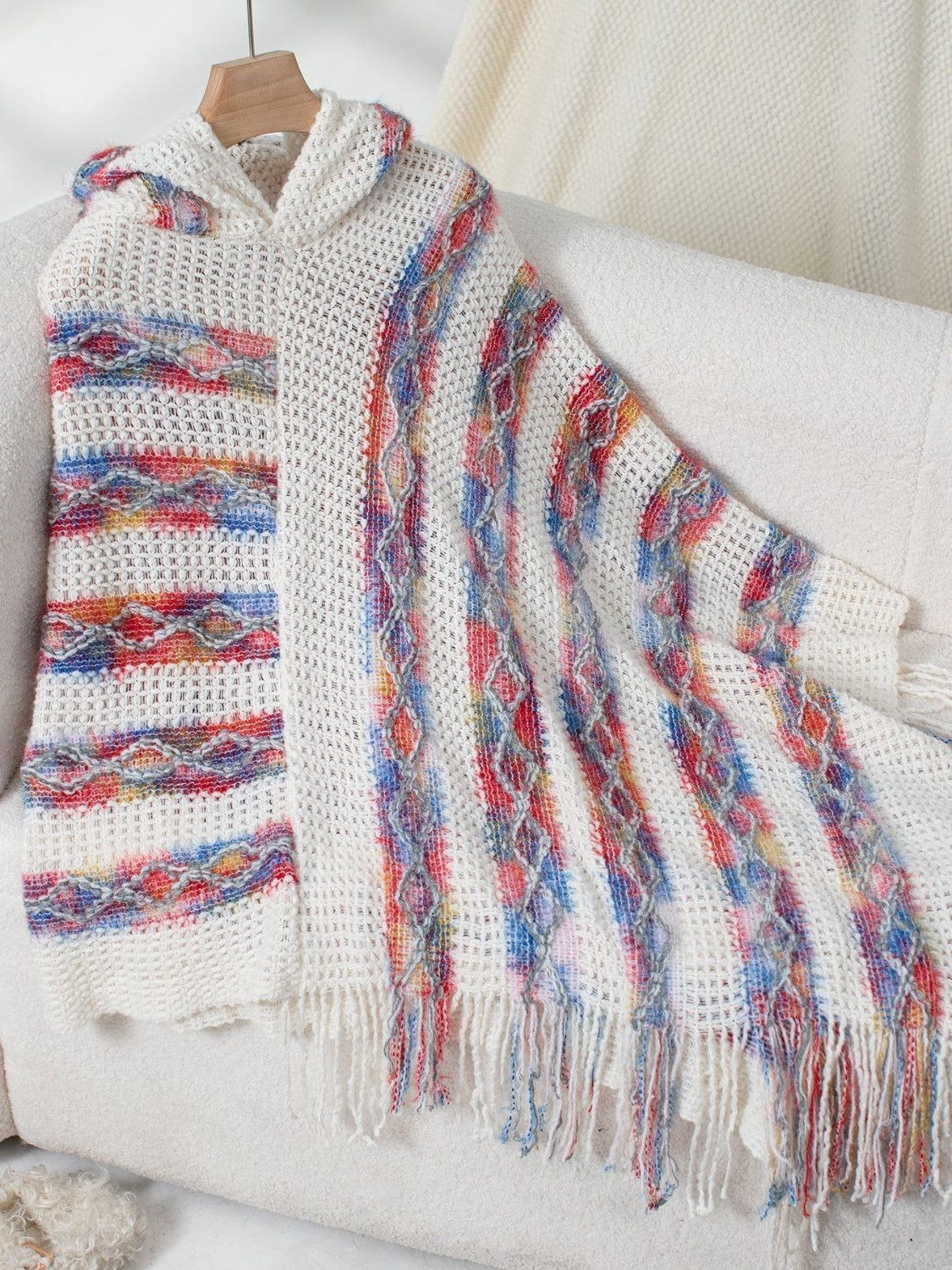 White knit hooded cape with colorful striped pattern and fringe detail