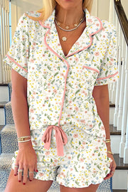 Ivory pajama set with pink trim, featuring a floral print, button-up top, and ruffled shorts with a bow.