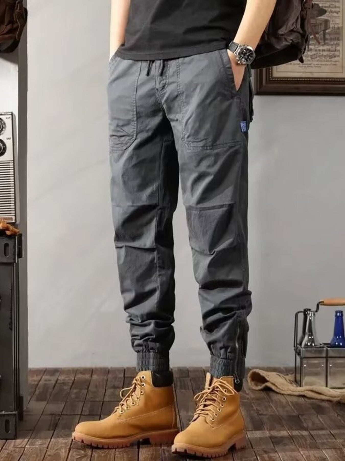 Men's grey cargo jogger pants with zippered ankles and multiple pockets.