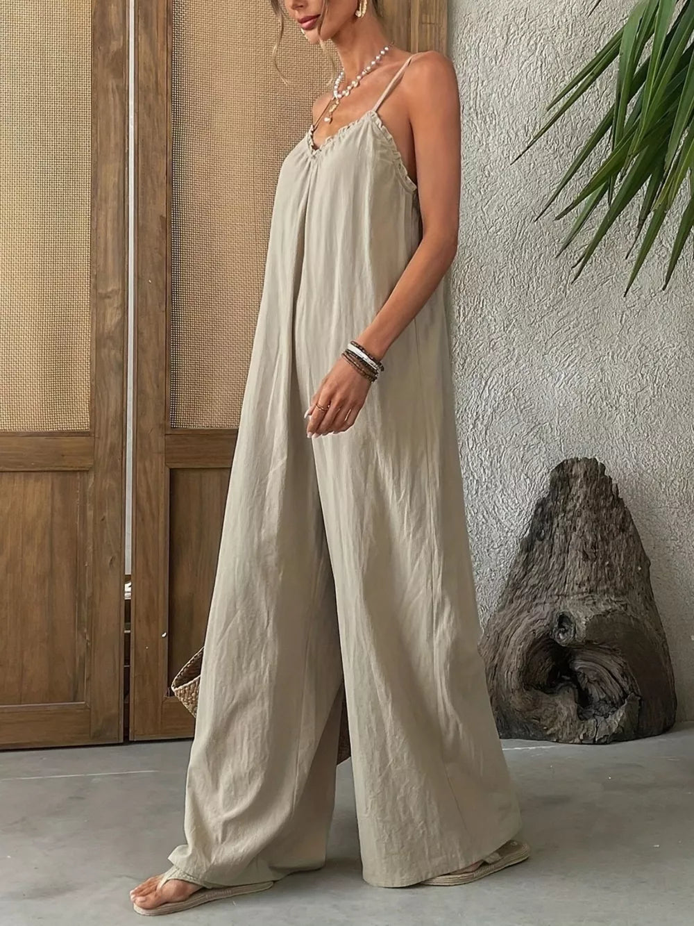 Sleeveless frill-trimmed beige jumpsuit with wide legs and spaghetti straps.