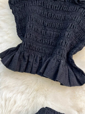 Black eyelet crop top with ruffled hem and smocked texture.