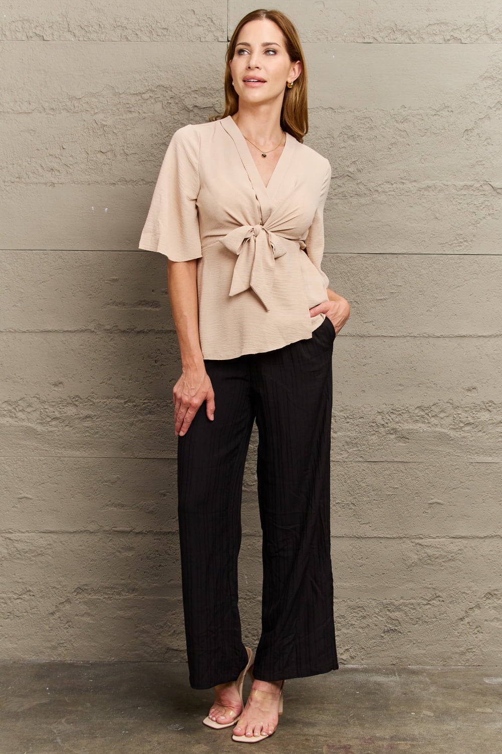 Light apricot wrap-front blouse with tie waist and flutter sleeves, styled with black pants.