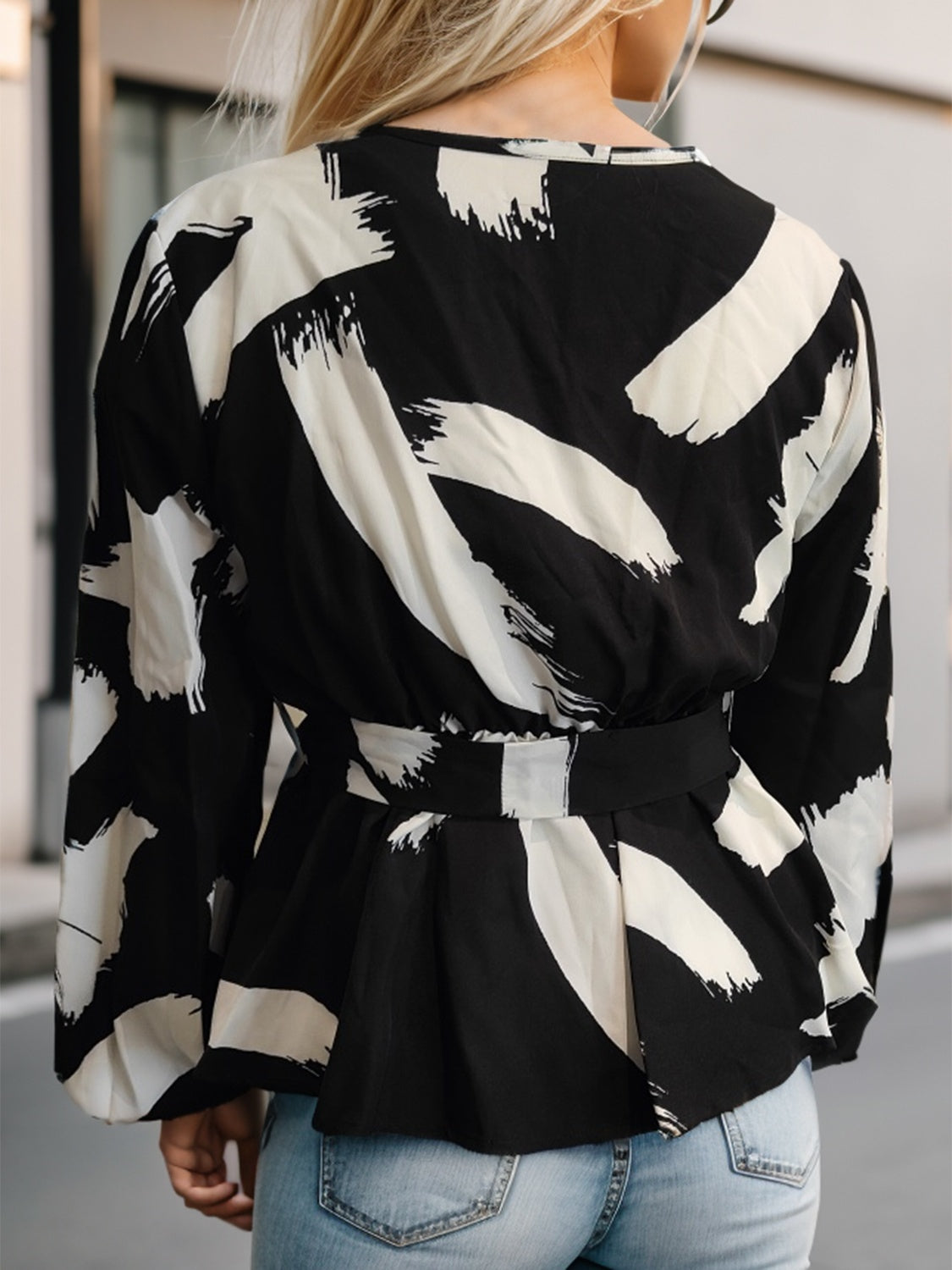 Black and white brushstroke wrap blouse with belted peplum waist and lace trim detail.