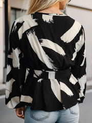 Black and white brushstroke wrap blouse with belted peplum waist and lace trim detail.