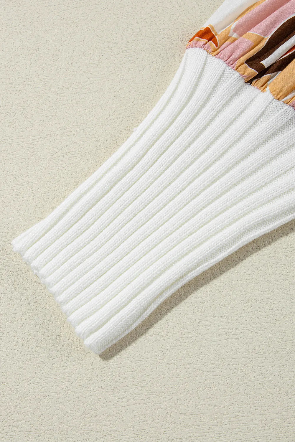 White ribbed knit sweater sleeve with a colorful abstract floral print fabric detail at the cuff.