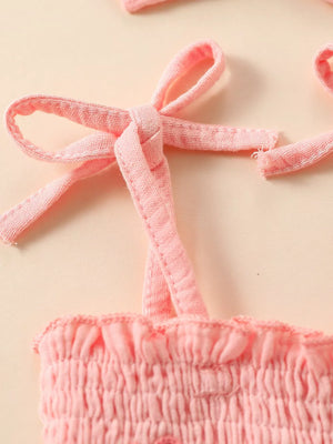 Pink smocked baby bodysuit with tie straps and matching headband detail.