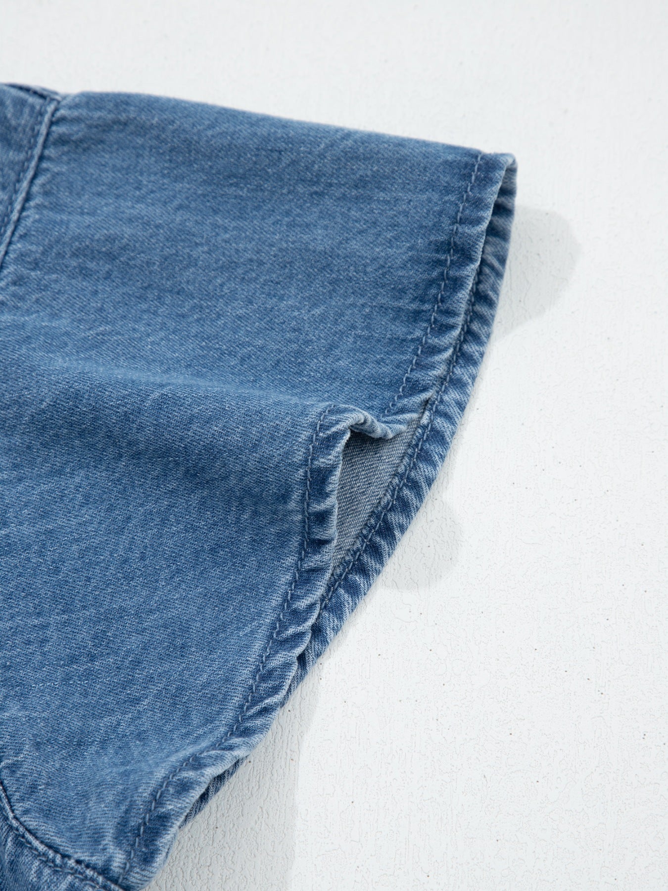 Denim button-up shirt detail showing a rolled sleeve cuff with visible stitching.